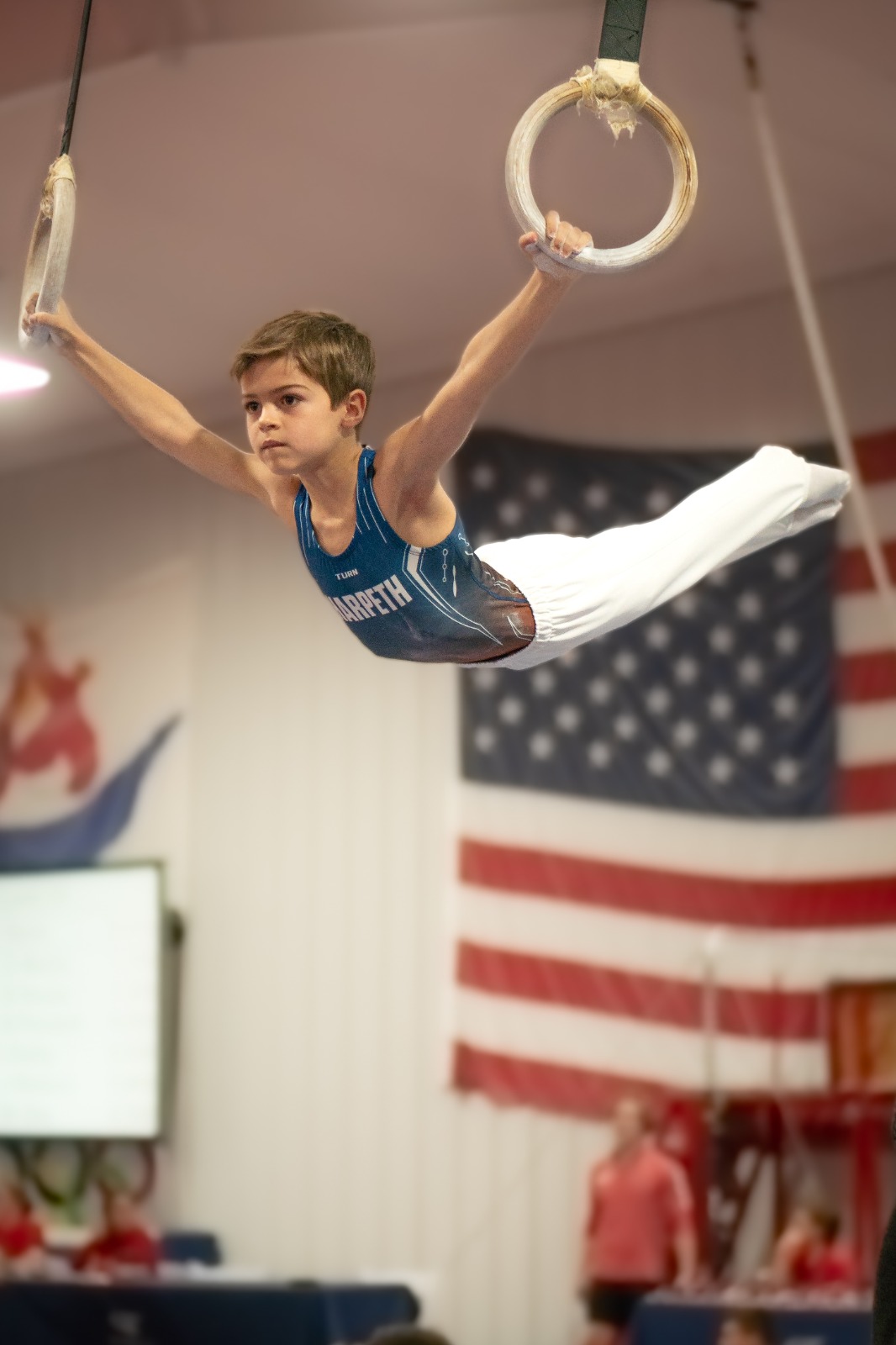 A boy on the Competitive Team is pictured in perfect form on the rings during a competition.