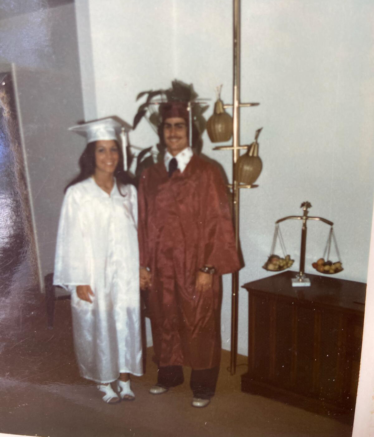 Glenda and Scott Webster on their graduation day from Franklin High School in 1974. Glenda stands on the left in a white cap and gown. Scott stands on the right in a red cap and gown.