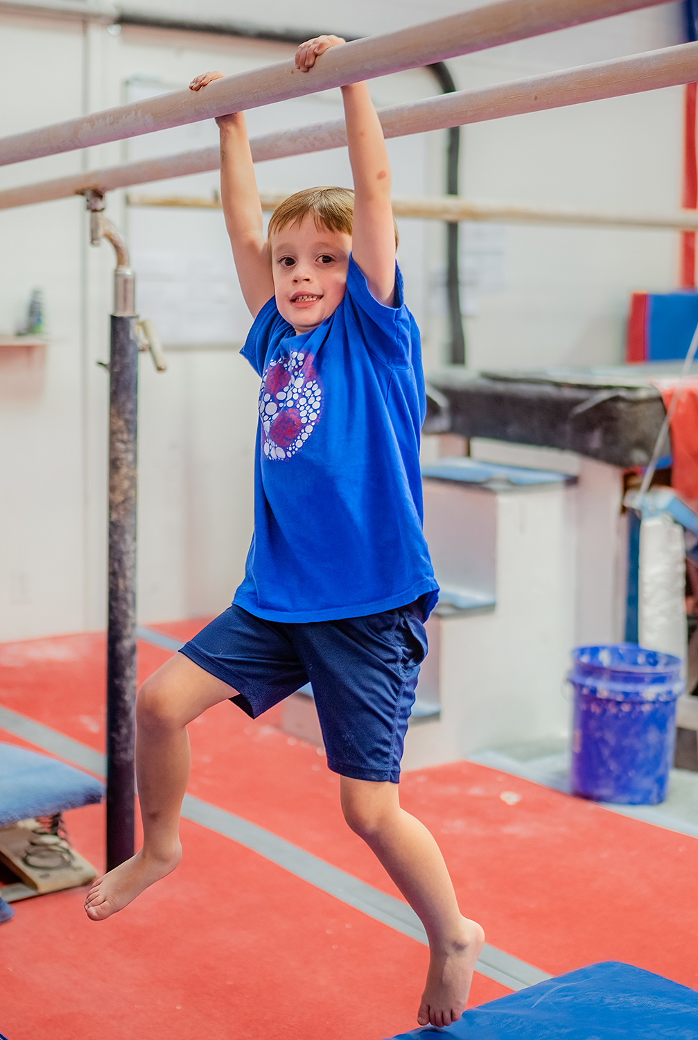 A young boy hands from the parallel bars during a class.