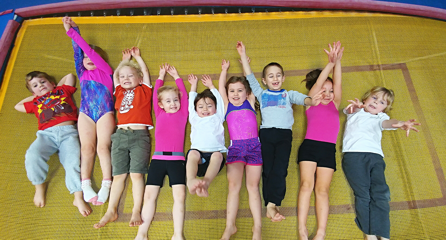 Nine young children lay in line smiling and laughing on the trampoline at a Harpeth Gymnastics event.