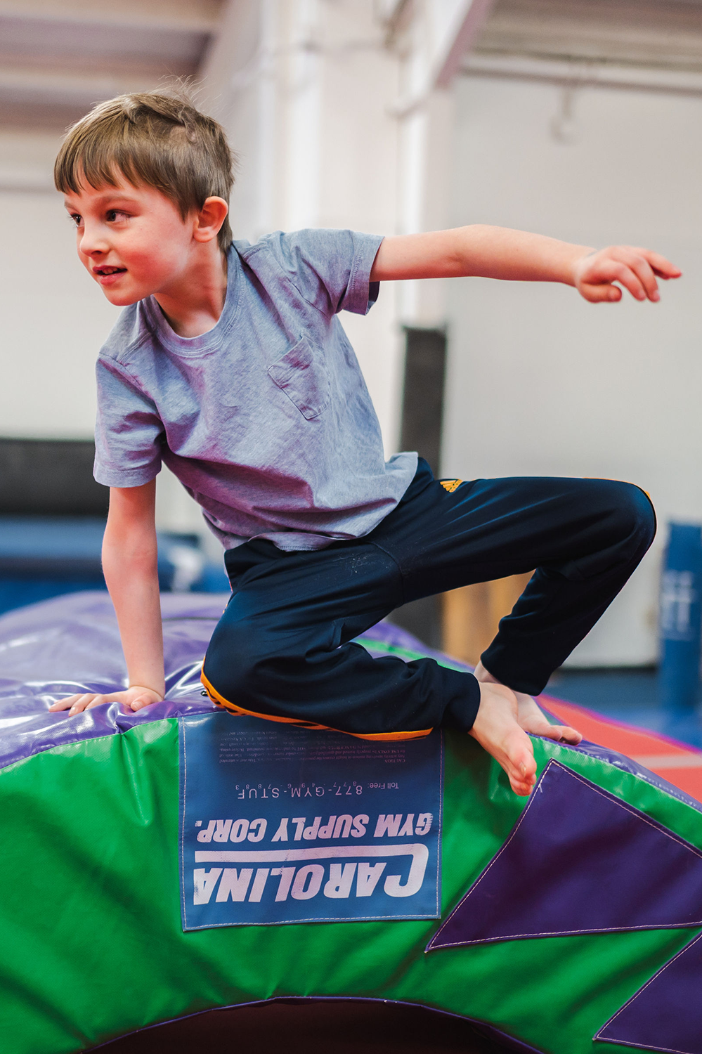 A young boy leaps off the edge of a soft play tumbling structure inside the gym.